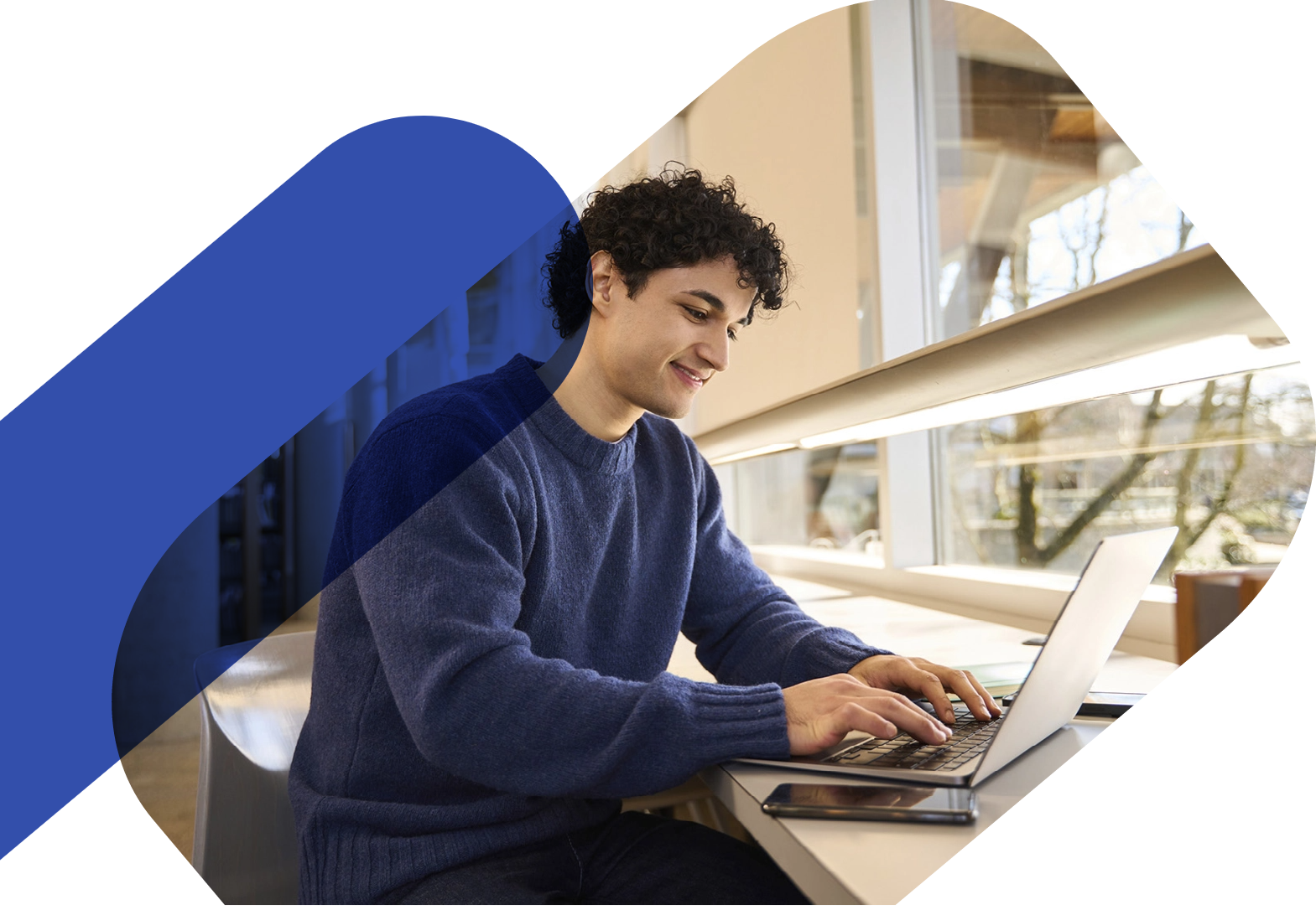 Homme travaillant sur un ordinateur portable près d'une fenêtre avec un élément graphique bleu en surimpression